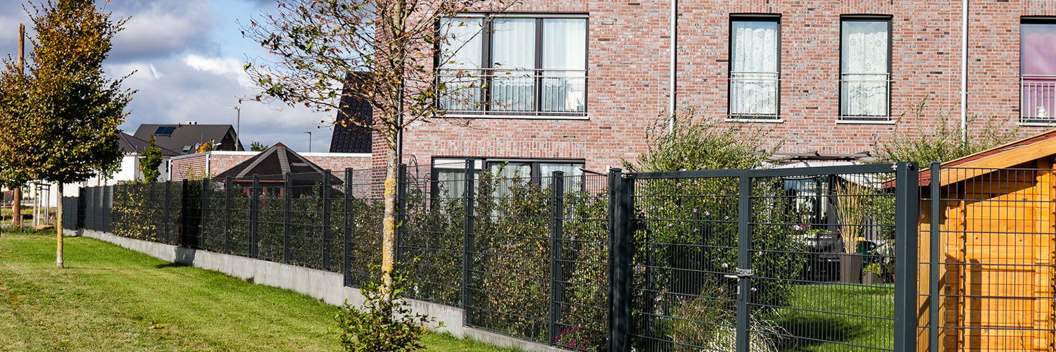 In rot geklinkertes Haus mit anthrazitem Zaun als Begrenzung